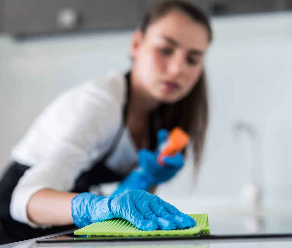 Young woman in blue gloves wiping a kitchen counter with a green cloth in a home in Orlando