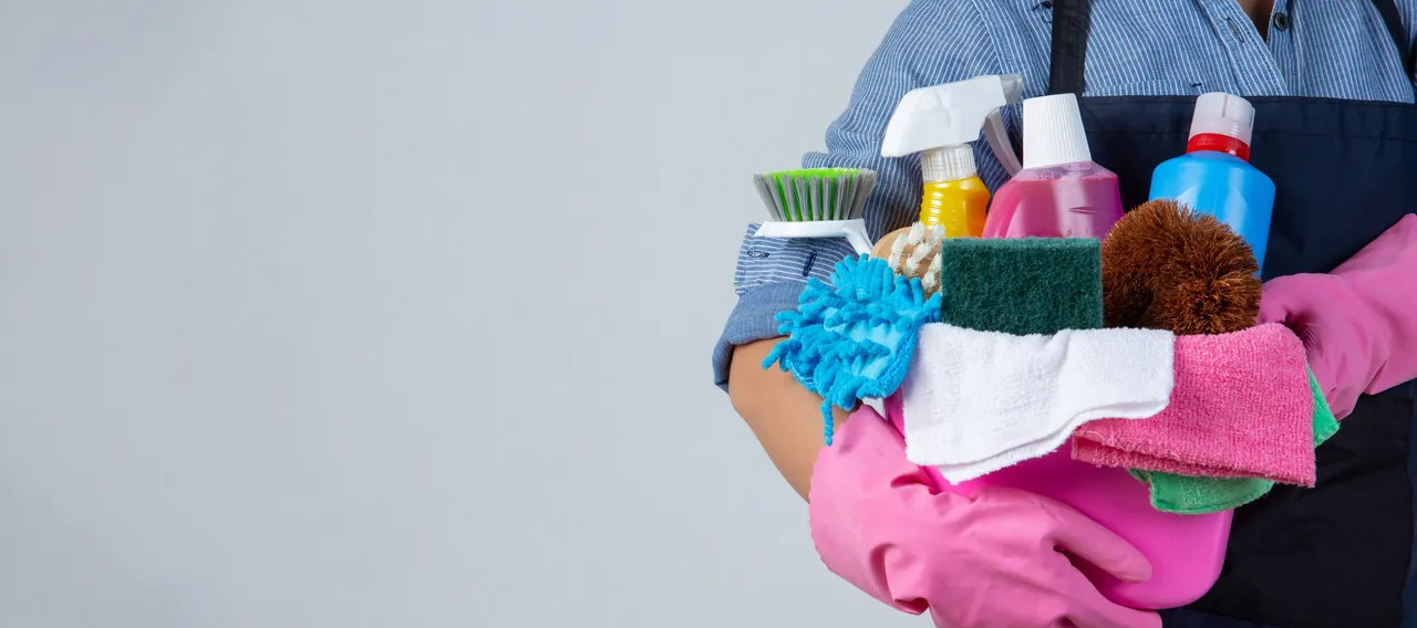 Our story: cleaning with purpose in Orlando, FL Cleaning professional in an apron and pink gloves holding a basin of products, brushes and cloths for cleaning homes in Orlando