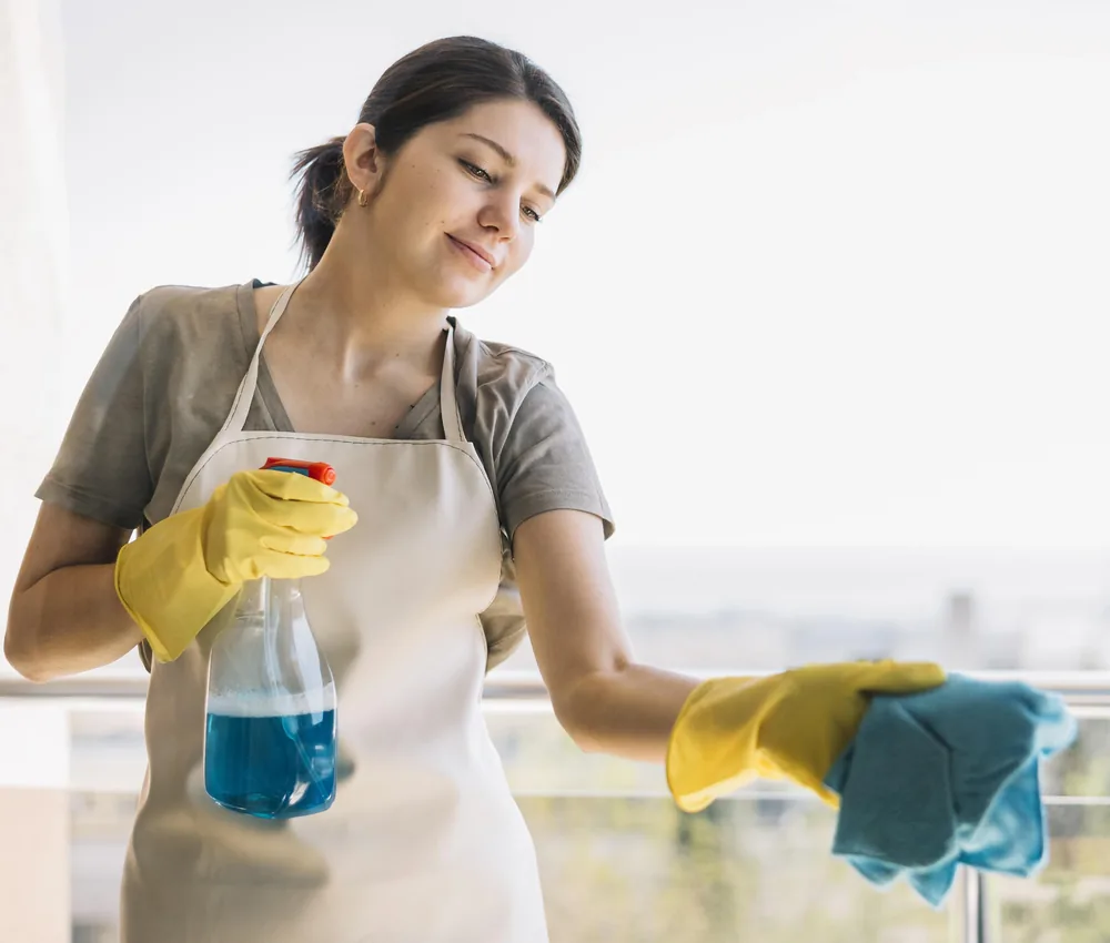 Profesional de limpieza sonriente con guantes amarillos y atomizador limpiando en una casa de Orlando