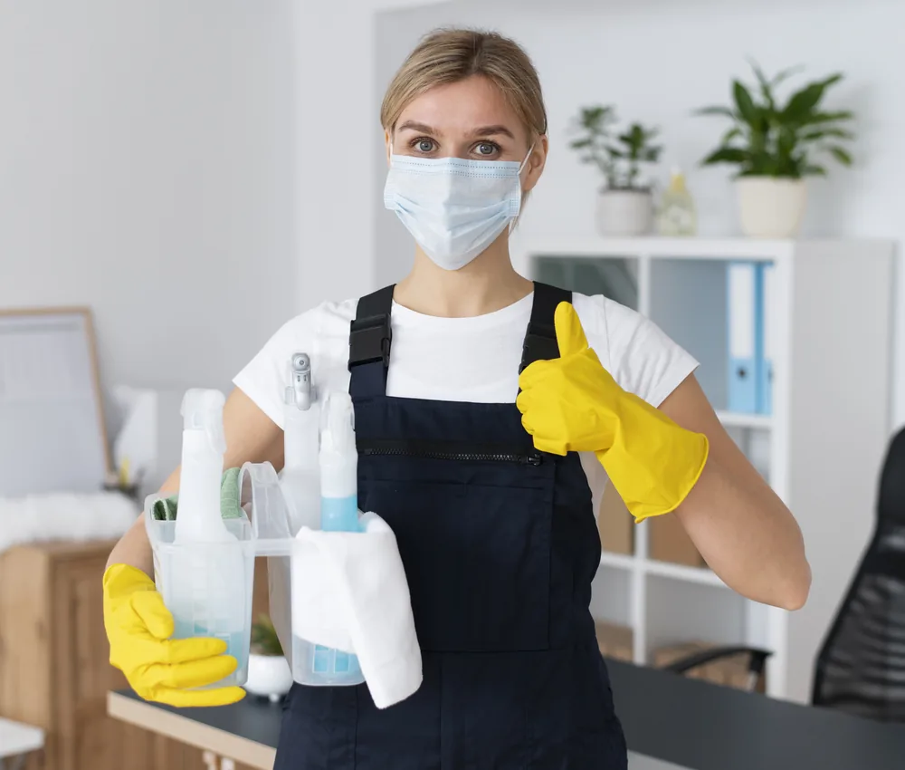 Profesional de limpieza con mascarilla y guantes amarillos sostiene productos de limpieza en una oficina en Orlando